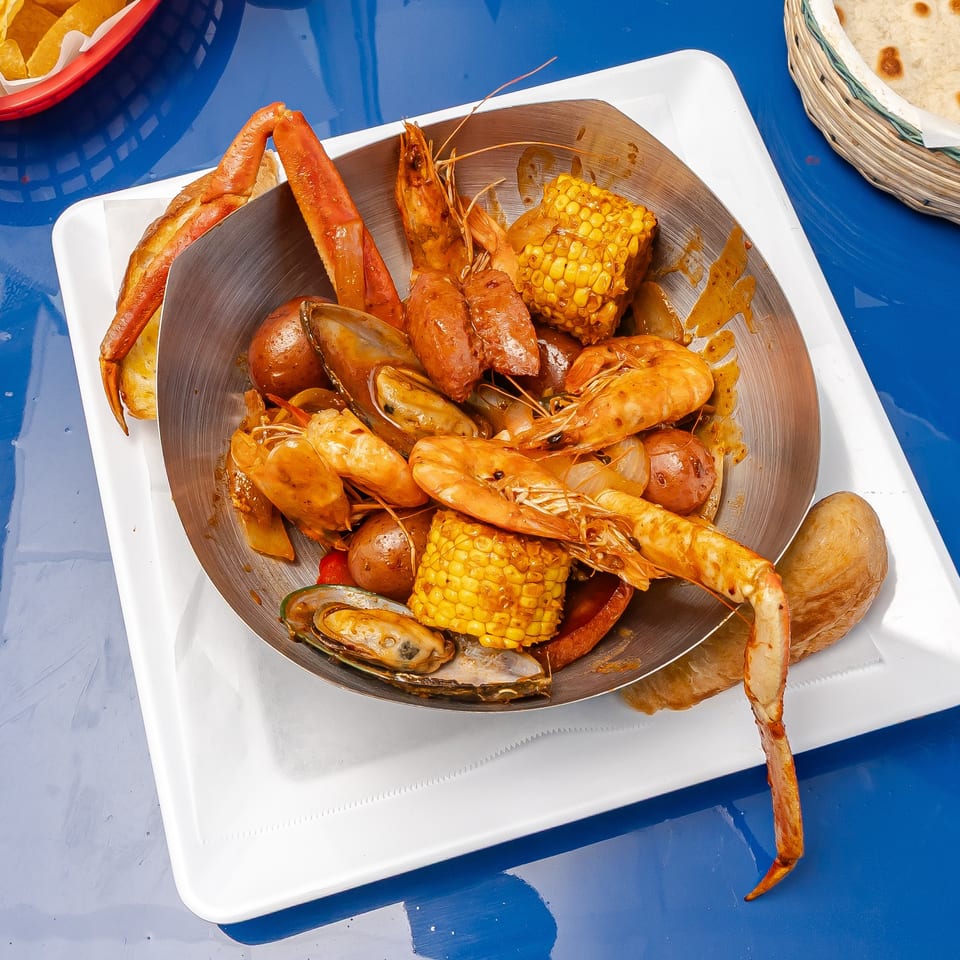 Seafood boil platter with shrimp, crab legs, mussels, sausage, potatoes, and corn on a blue table.