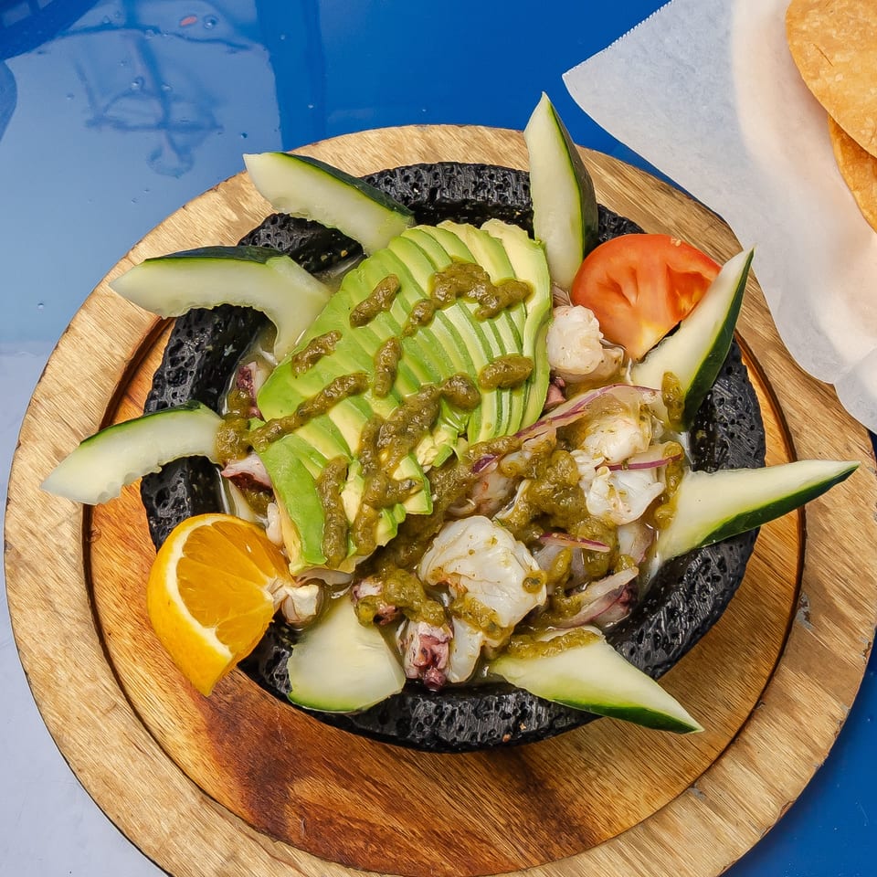 Seafood salad topped with sliced avocado, cucumber, tomato, citrus, and green dressing on a wooden platter.