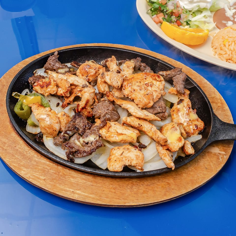 Sizzling skillet of grilled chicken, beef, onions, and peppers served with Mexican rice, salad, and lime.